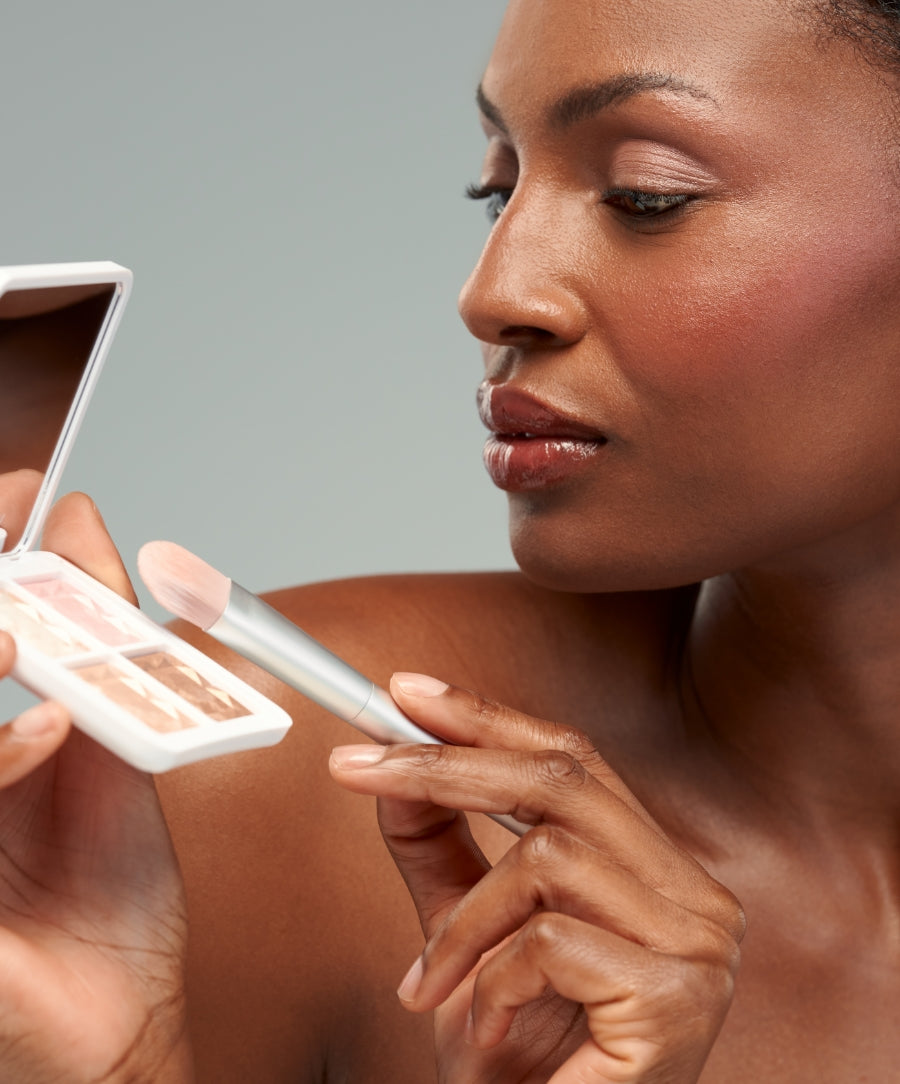 Close-up of a woman applying makeup using the ReDimension Daily Glow Palette with a brush, highlighting clean beauty and natural ingredients for a radiant complexion.
