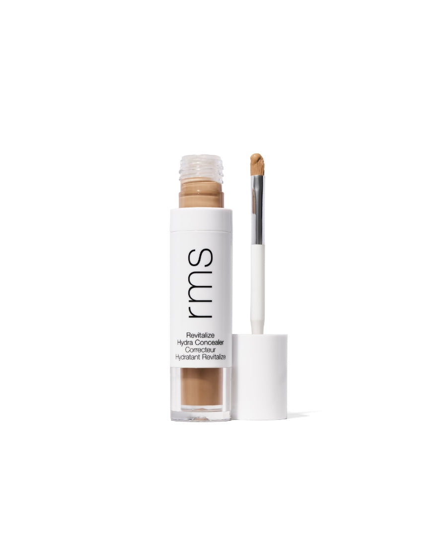 Open tube of Revitalize Hydra Concealer by RMS Beauty with visible creamy beige concealer and attached applicator brush against a white background