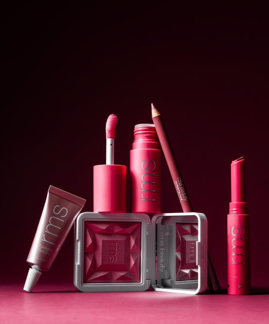 A vibrant assortment of RMS Beauty makeup products in various shades of pink and red arranged against a deep rose background, showcasing Color Capsule: The Rosé Edit with clean, cruelty-free ingredients and sustainable packaging.