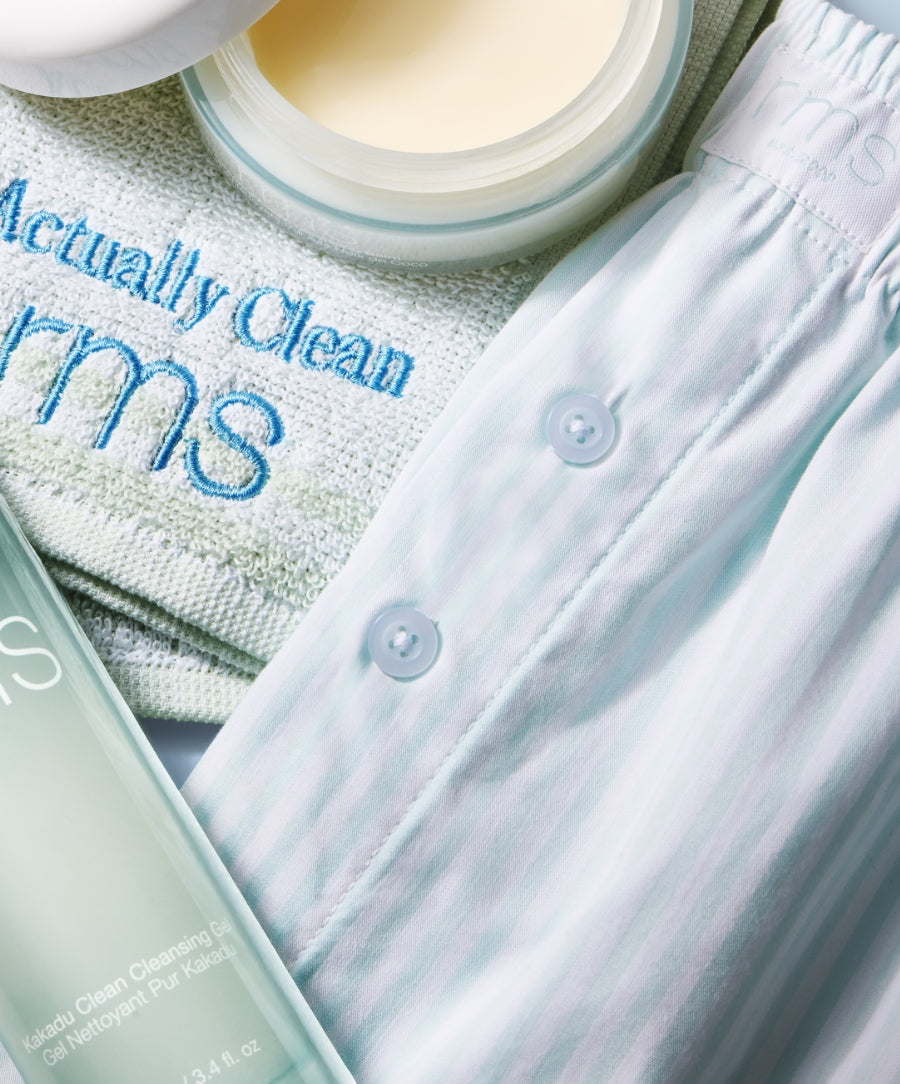 Light pastel striped Striped Sleep Shorts with buttons, placed next to skincare products and a towel embroidered with RMS, emphasizing clean beauty and natural ingredients.