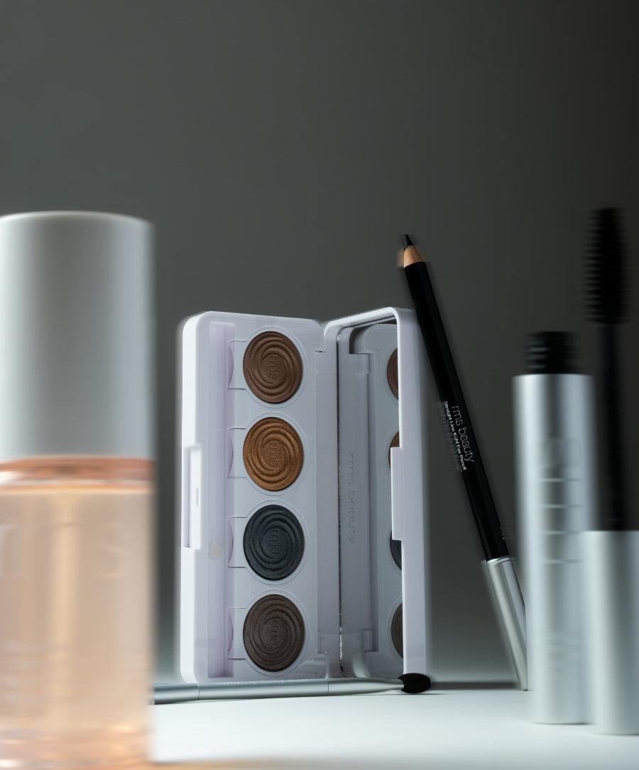 The Signature Artistry Set featuring a palette of four earthy eyeshadows, a black eyeliner pencil, and a silver tube of mascara, displayed with soft natural lighting.