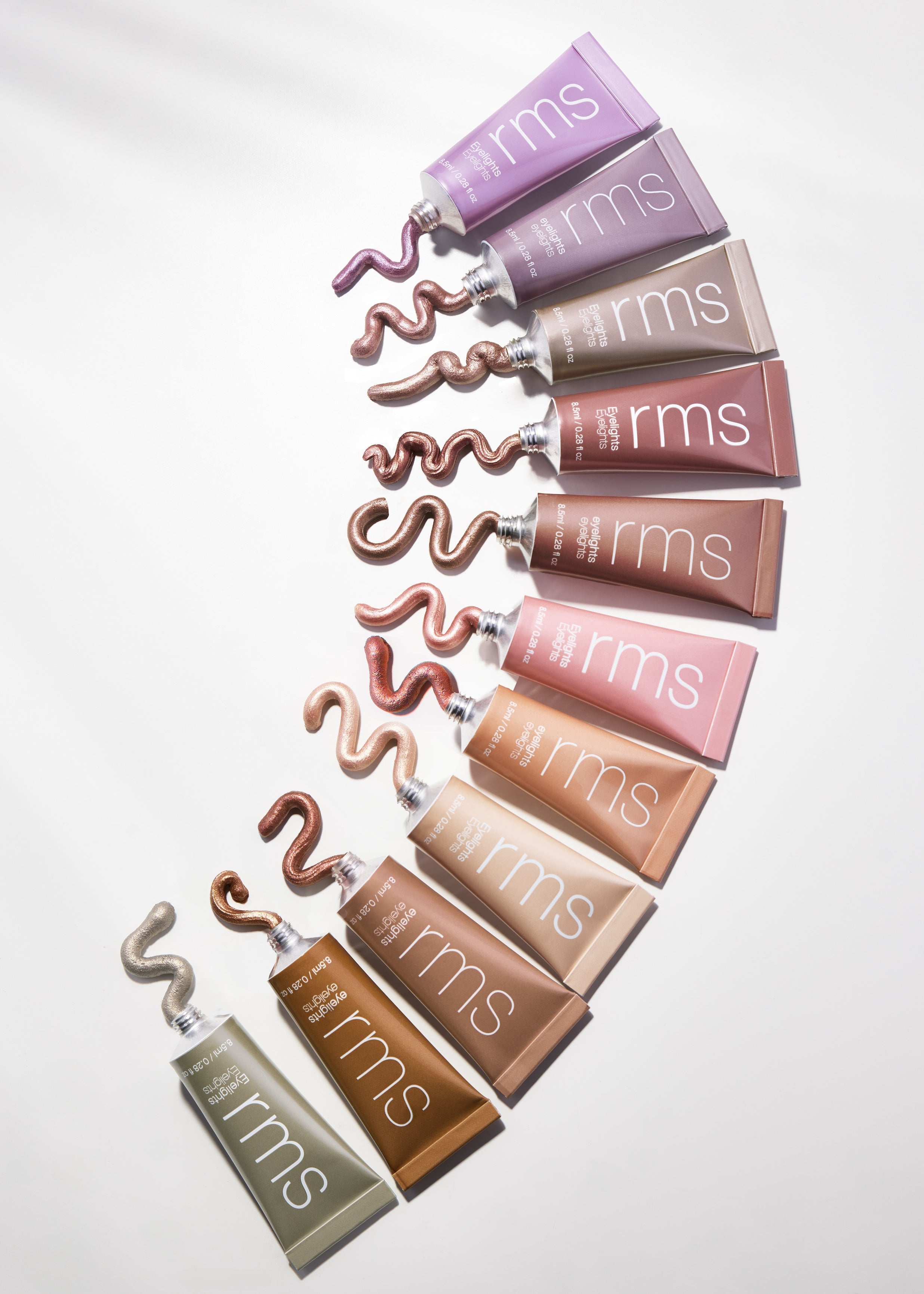 A selection of tubes with various shades of RMS Beauty Eyelights Cream Eyeshadow, each with a swirled cream eyeshadow sample extending from the tube, showcasing a range of natural and metallic colors.
