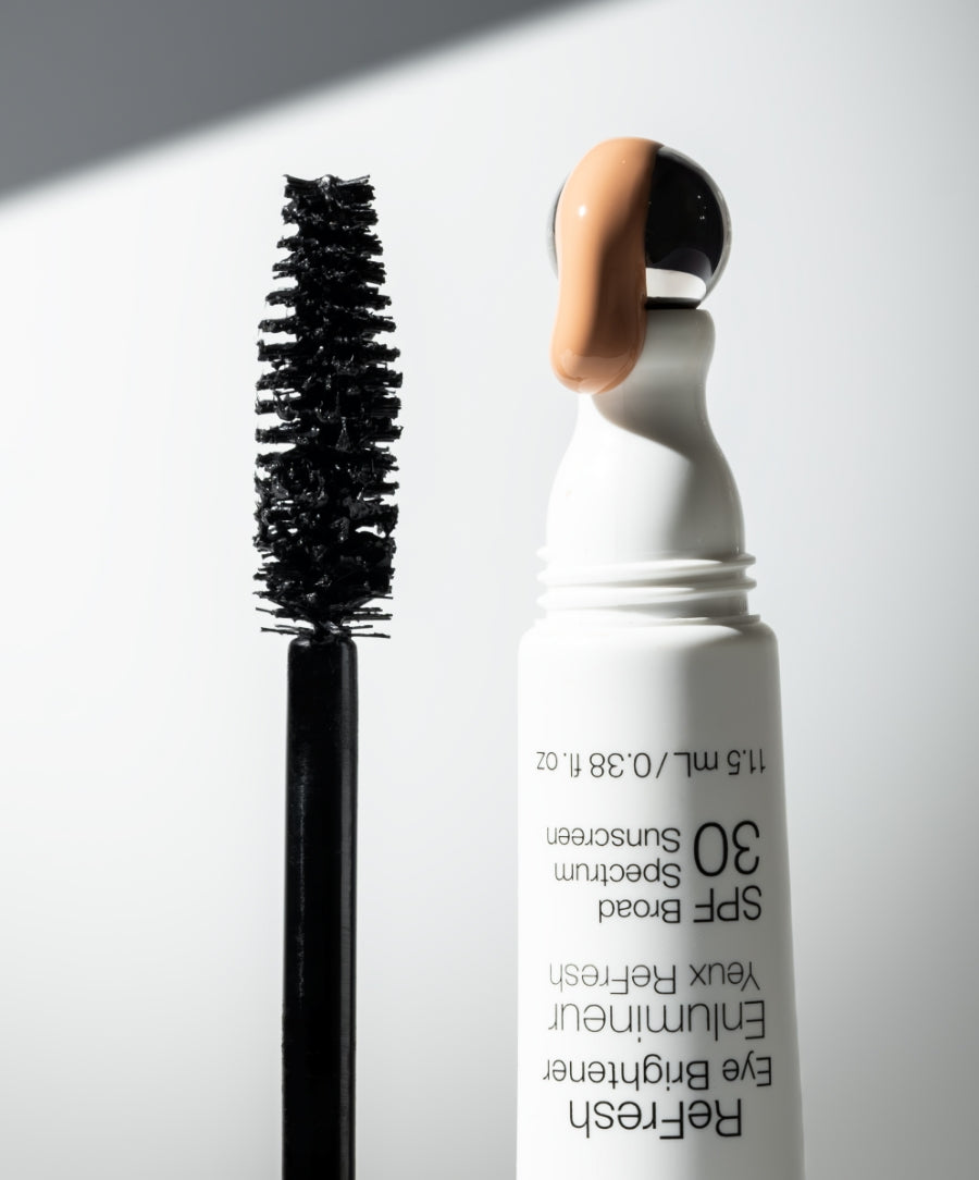 Close-up of a mascara wand and an open tube with beige cream on the cap, representing The Wide Awake Duo with natural ingredients for clean beauty and skincare infused makeup.