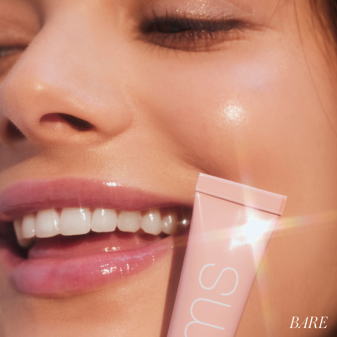 Close-up of a smiling woman with glowing skin holding a pink tube of Liplights Cream Lip Gloss near her mouth, highlighting the product’s smooth, glossy finish and clean beauty appeal.