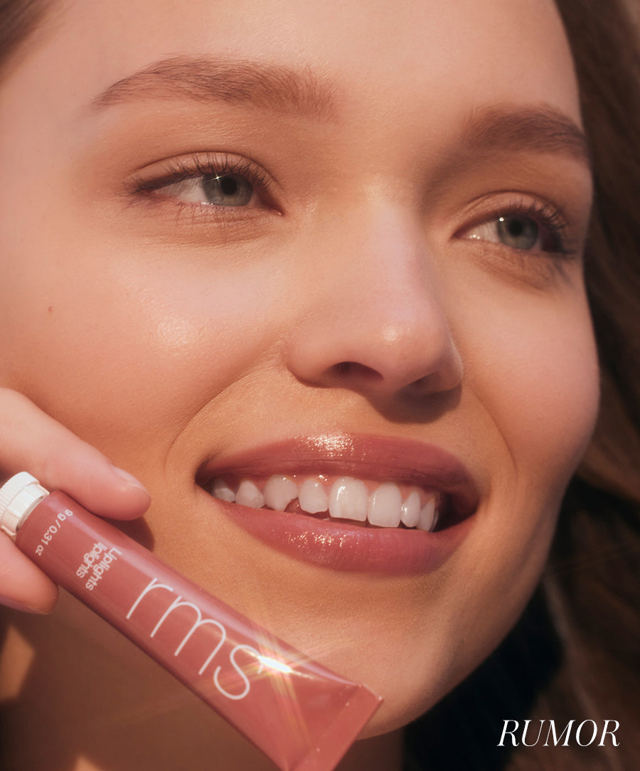 Close-up of a smiling woman with natural makeup holding a tube of Liplights Cream Lip Gloss in a soft, rosy shade, showcasing smooth, glossy lips and radiant skin.
