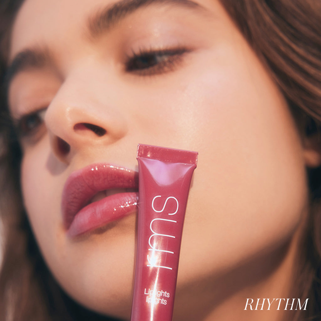 Close-up of a woman with glossy pink lips holding a tube of Liplights Cream Lip Gloss near her face, emphasizing smooth, hydrated skin and a clean beauty look.