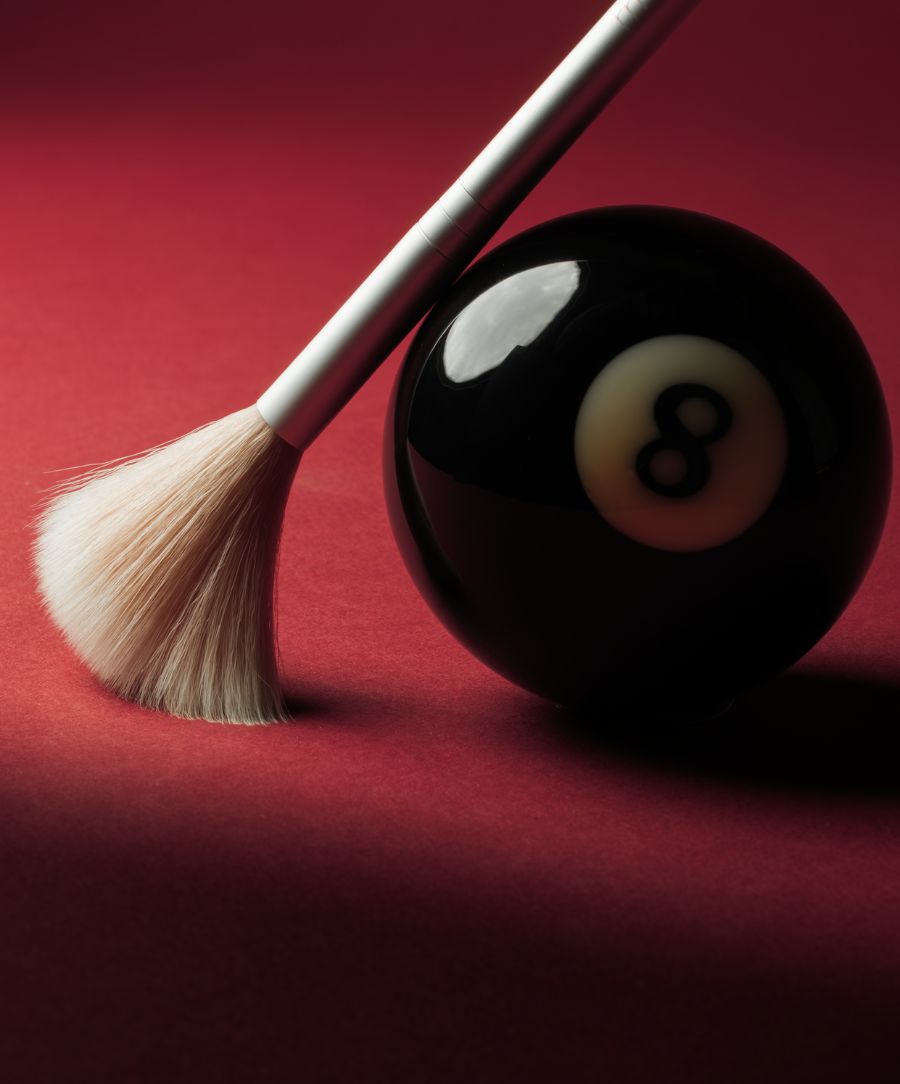 Skin2Skin Classic Fan Brush with soft, delicate bristles resting against a black eight ball on a deep red background, highlighting the brush’s clean beauty and natural ingredients appeal.