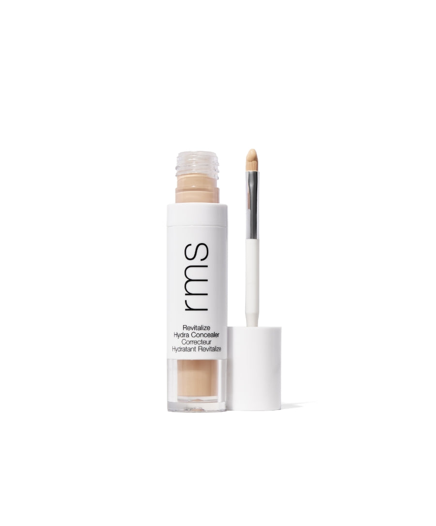 Open tube of Revitalize Hydra Concealer with built-in applicator wand showing natural beige cream formula in clear and white packaging labeled rms, highlighting clean beauty and skincare infused makeup.