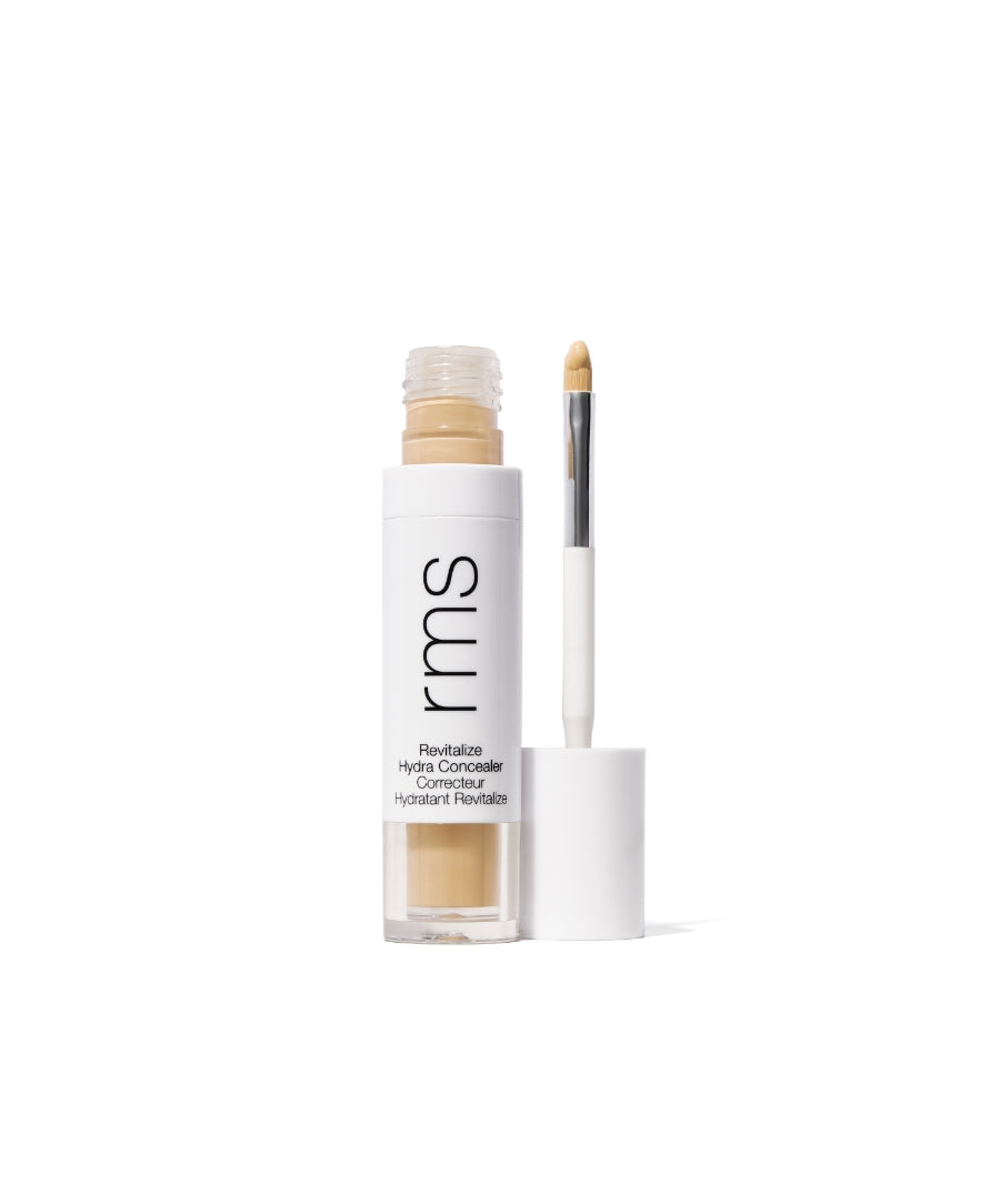 Open tube of Revitalize Hydra Concealer with visible beige cream and attached applicator brush, featuring minimalist white and black packaging for clean beauty makeup.