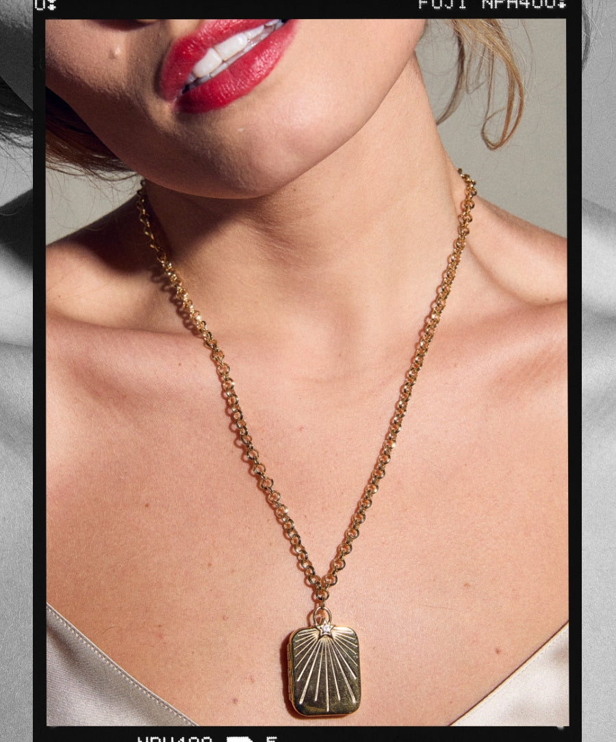 Close-up of a woman wearing a gold pendant necklace with a rectangular locket, showcasing the HART x RMS: Lip2Cheek Locket with clean beauty and sustainable packaging influence.