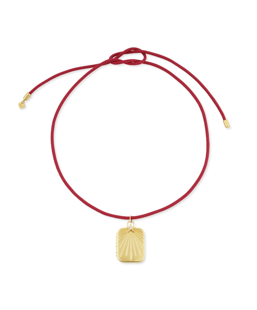 HART x RMS: Lip2Cheek Locket with a gold rectangular pendant featuring a sunburst design on a red adjustable cord necklace, reflecting clean beauty and sustainable packaging.