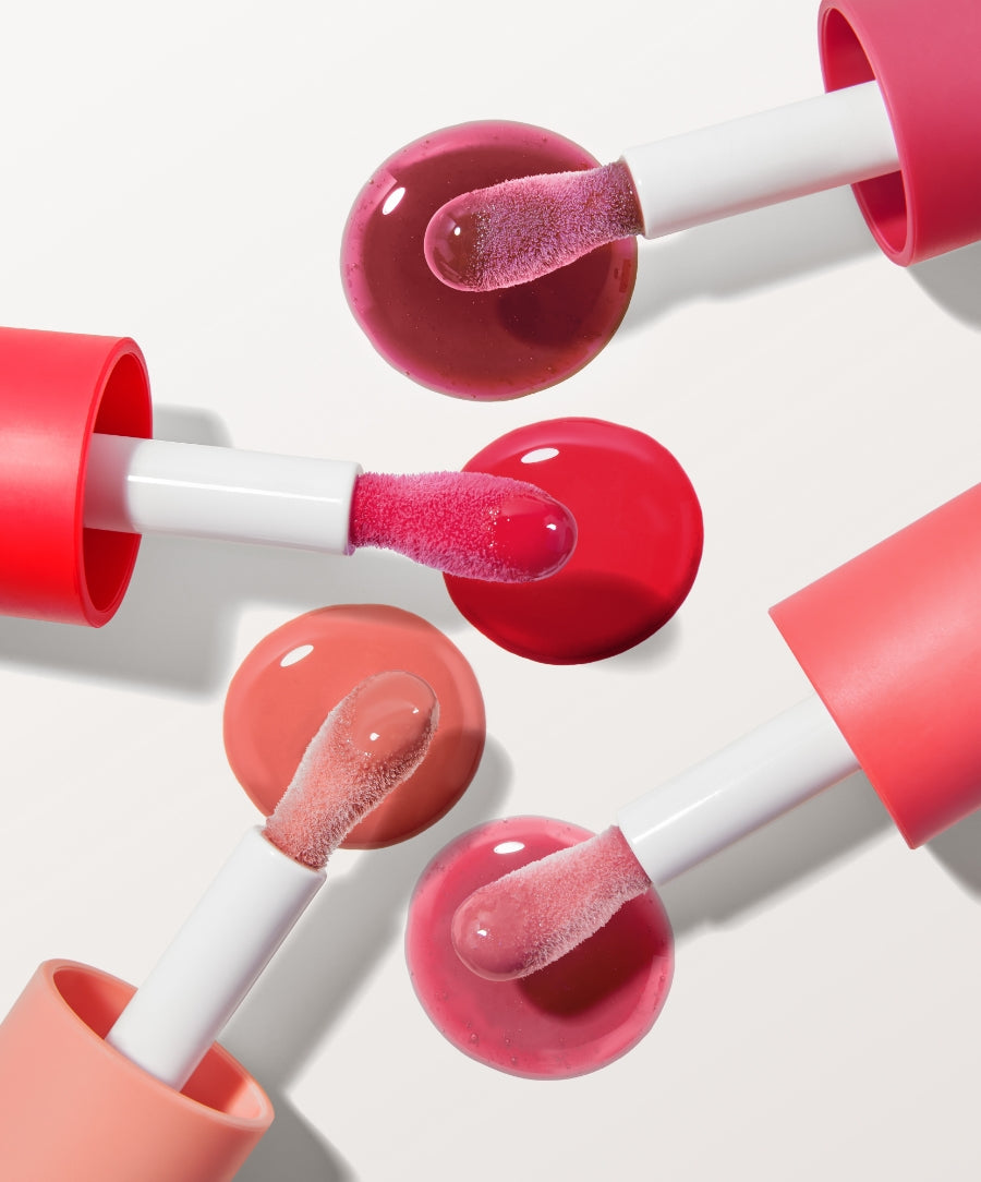 Close-up of four Legendary Lip Oil applicators with glossy, vibrant lip oils in shades of pink, red, and peach, highlighting natural ingredients and clean beauty appeal.