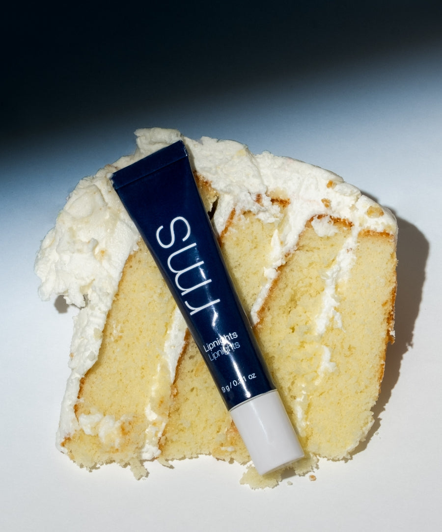 Lipnights Overnight Lip Mask tube resting on a slice of vanilla cake with white frosting, highlighting the product's smooth texture and nourishing qualities.
