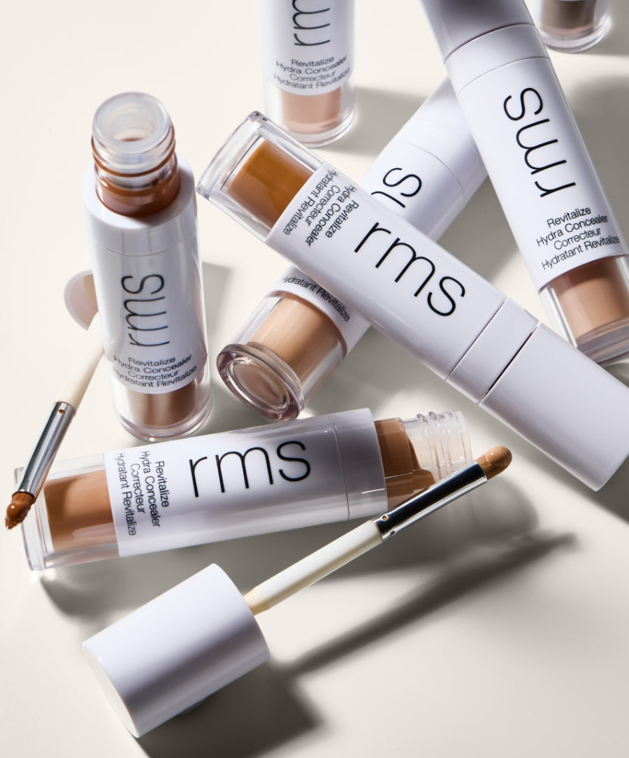 Several tubes of Revitalize Hydra Concealer with some open showing the applicator, arranged on a light background highlighting the natural shades and sleek white packaging.