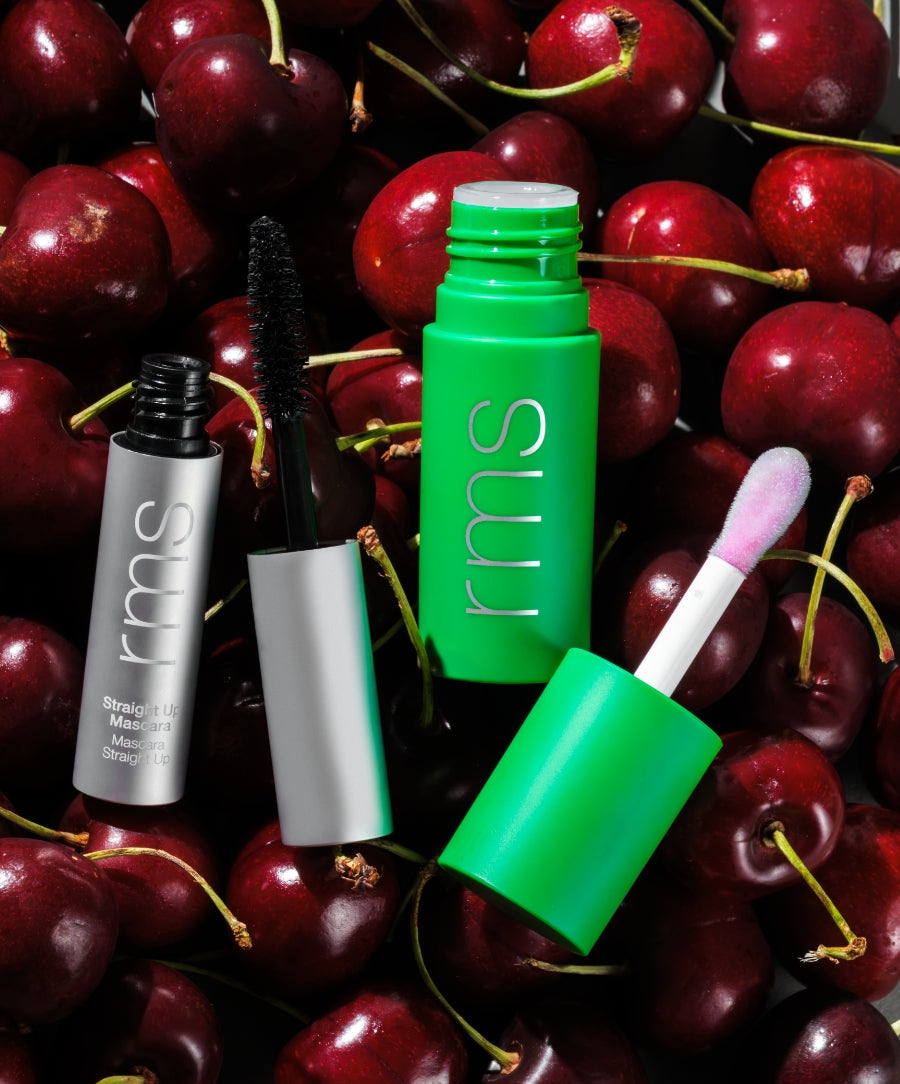 The Lip & Lash Duo: Volumizing Mascara + pH Tinted Lip Oil displayed with mascara wand and lip oil applicator on a background of fresh cherries emphasizing natural ingredients and clean beauty.