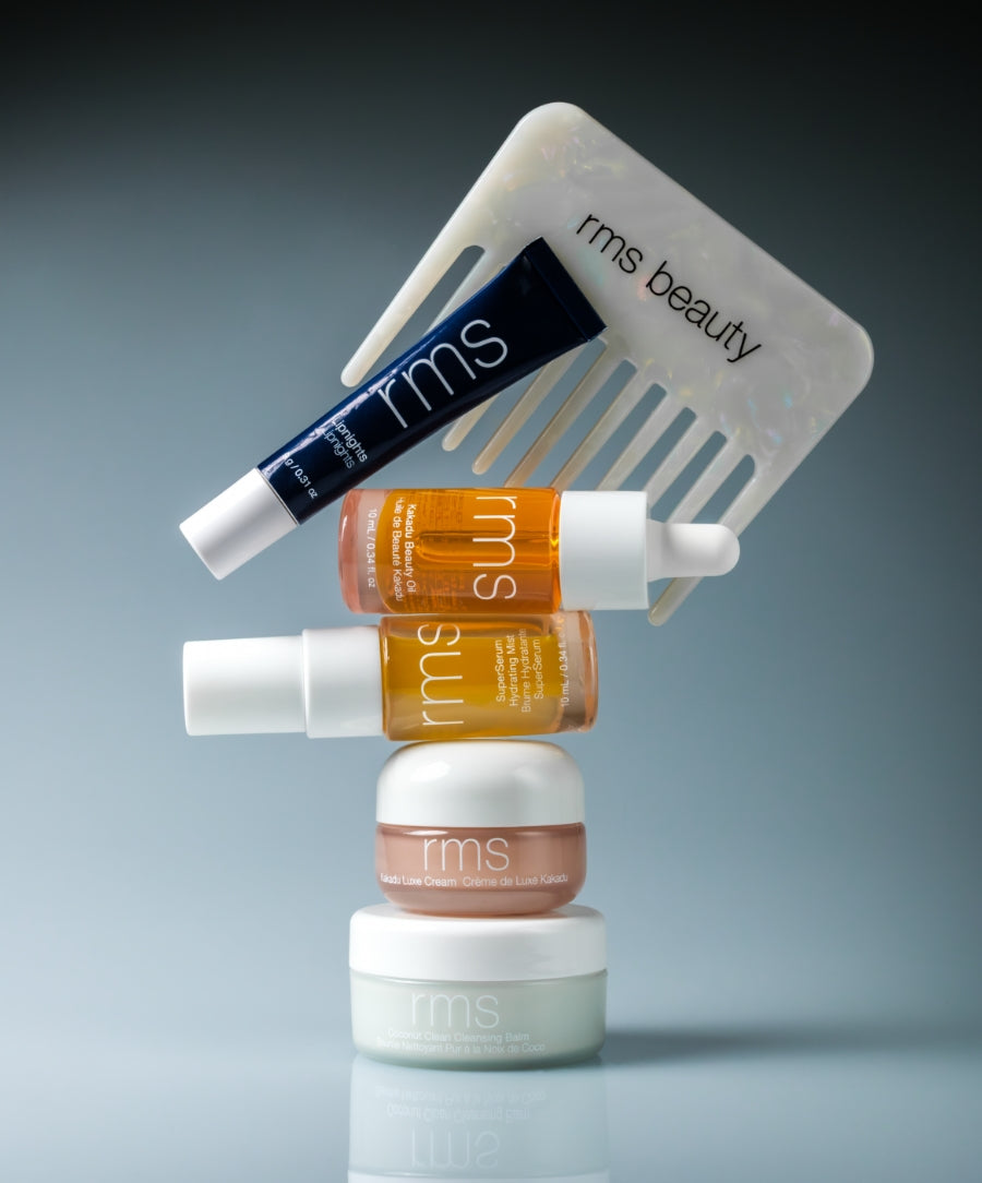 Stacked skincare products including serums, creams, and a comb branded rms beauty, showcasing natural ingredients and clean beauty in The Travel Skincare Set with sustainable packaging.