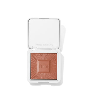 Compact powder makeup in warm brown shade with embossed sunburst design and "rms" logo on surface, in a white square case, ReDimension Hydra Bronzer.