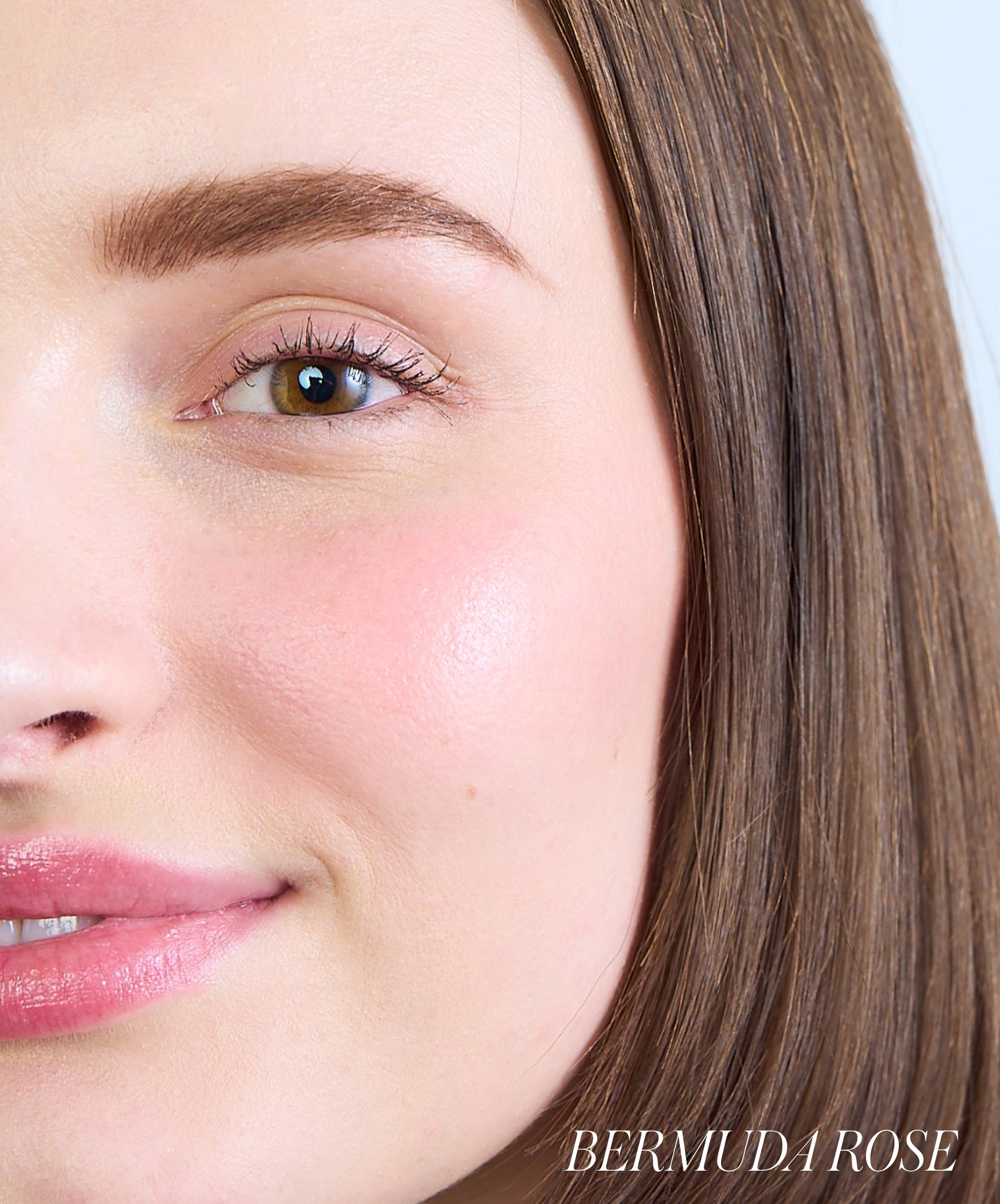 Close-up of a smiling woman with natural skin and subtle rosy cheeks wearing ReDimension Hydra Powder Blush in a soft Bermuda Rose shade, showcasing a clean beauty look.