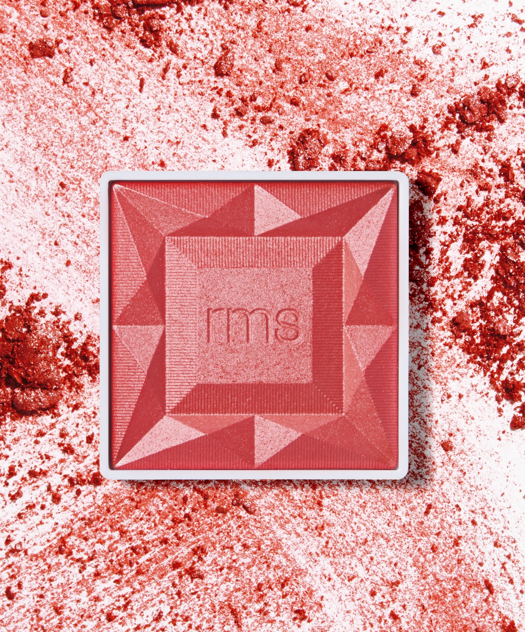 ReDimension Hydra Powder Blush in a geometric compact with vibrant red and pink tones, surrounded by crushed powder highlighting its smooth texture and rich pigmentation.