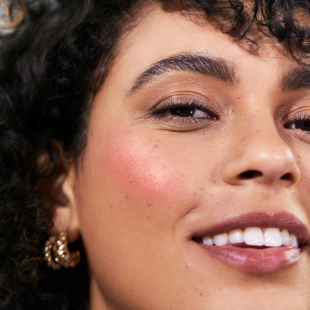 Close-up of a smiling woman with glowing skin wearing ReDimension Hydra Powder Blush, showcasing natural makeup with a soft rosy tint and radiant finish.