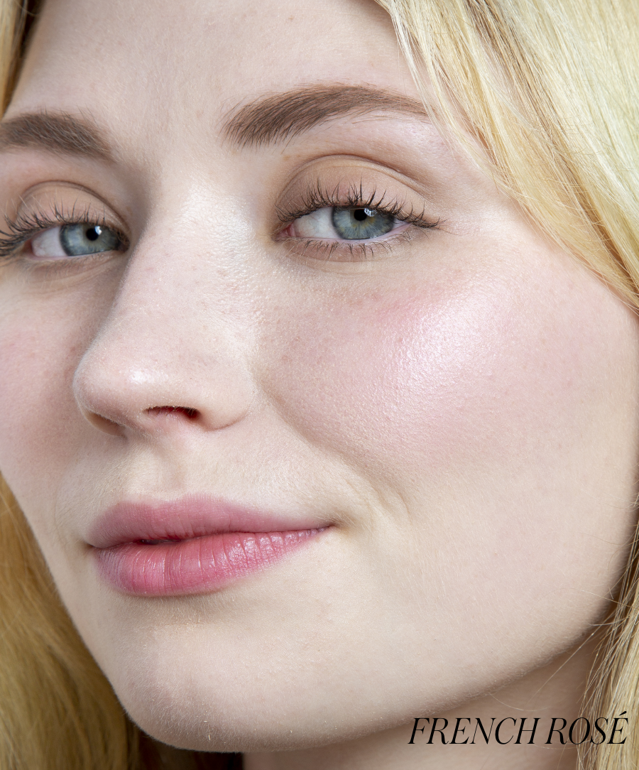 Close-up of a woman with fair skin and blue eyes wearing ReDimension Hydra Powder Blush in a soft French rosé shade, showcasing natural, radiant makeup with clean beauty appeal.