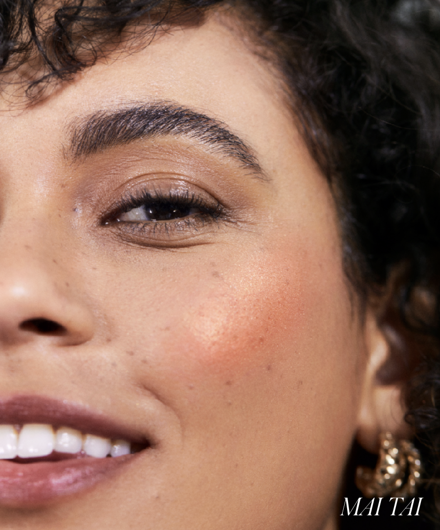 Close-up of a smiling woman with natural makeup showcasing a warm coral blush on her cheek, highlighting the radiant finish of ReDimension Hydra Powder Blush.