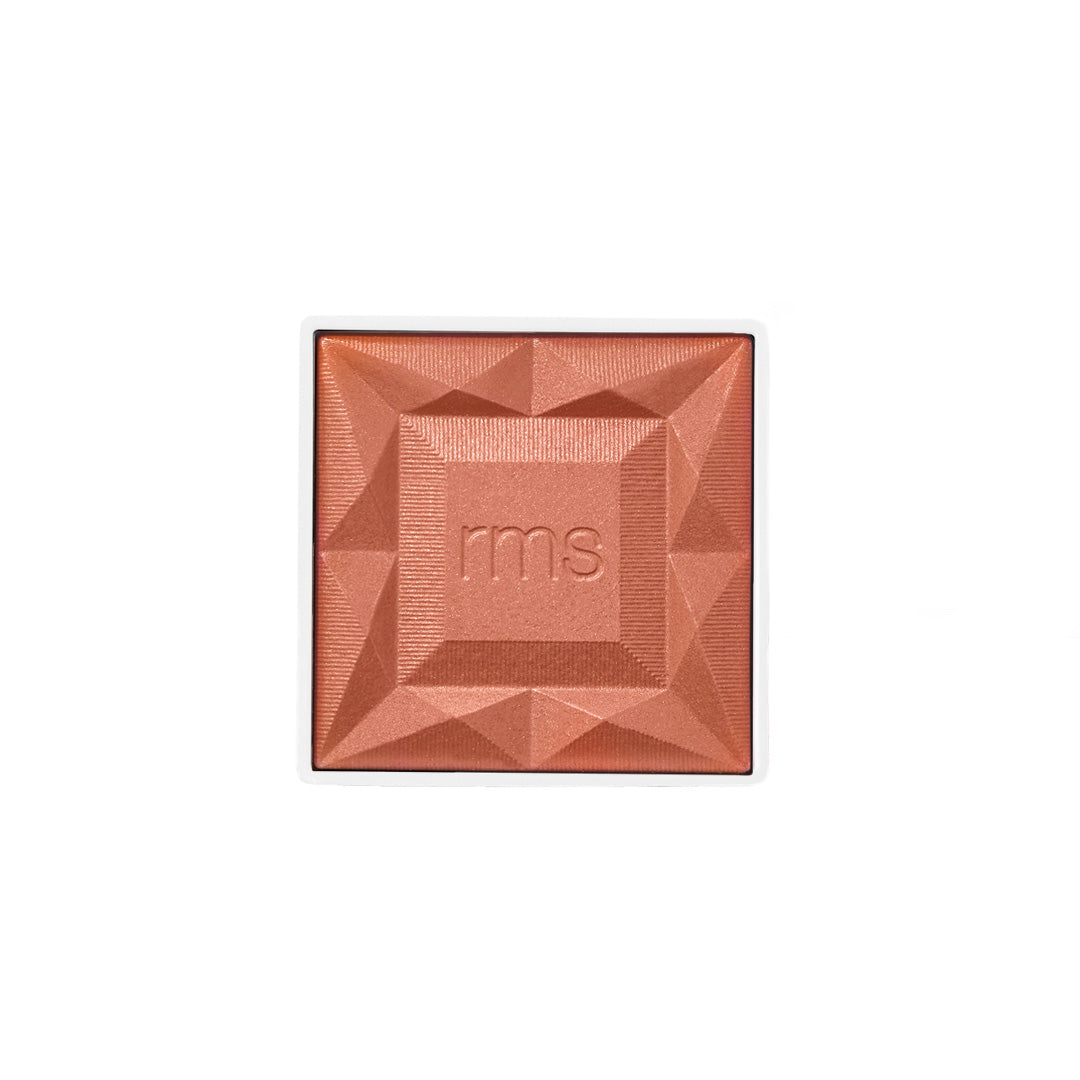 Close-up of a warm coral powder blush with geometric embossed design and the letters rms in the center, showcasing ReDimension Hydra Powder Blush in eco-friendly recyclable packaging.