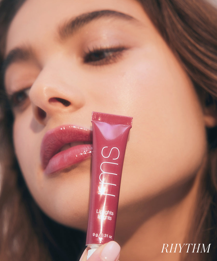 Close-up of a woman with glossy, natural lips holding a tube of Liplights Cream Lip Gloss, showcasing radiant, clean beauty and smooth skin.